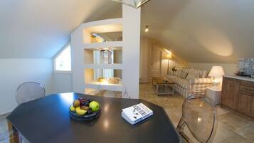 Una cocina moderna con una mesa de comedor, un frutero y un libro. Hay una sala de estar con un sofá y una lámpara.