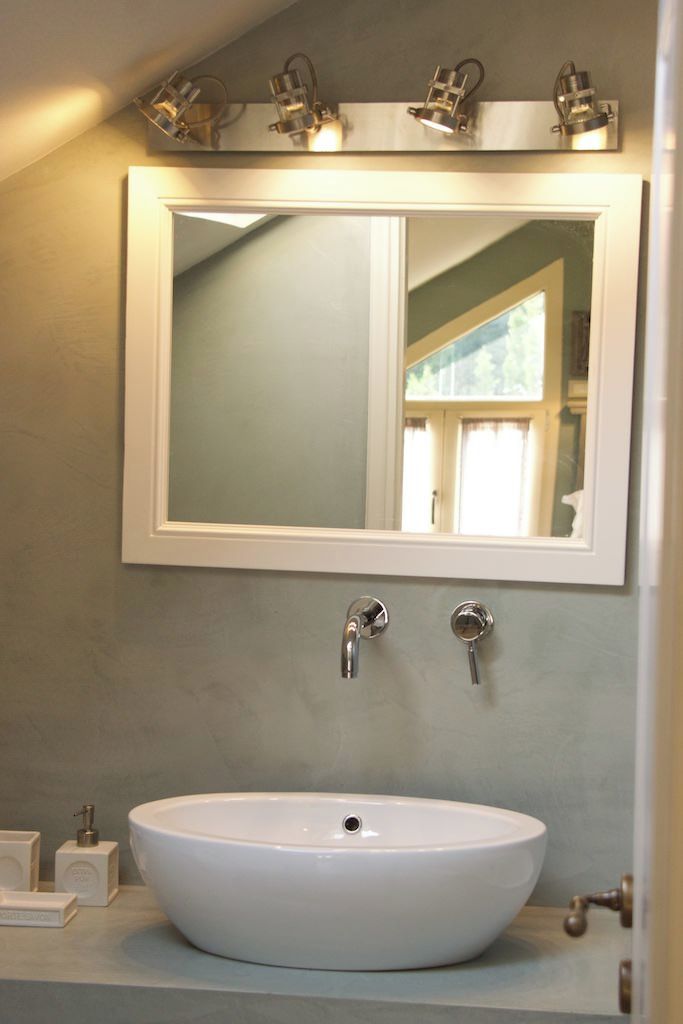 Un baño con un lavabo blanco, dos llaves y un espejo encima.
