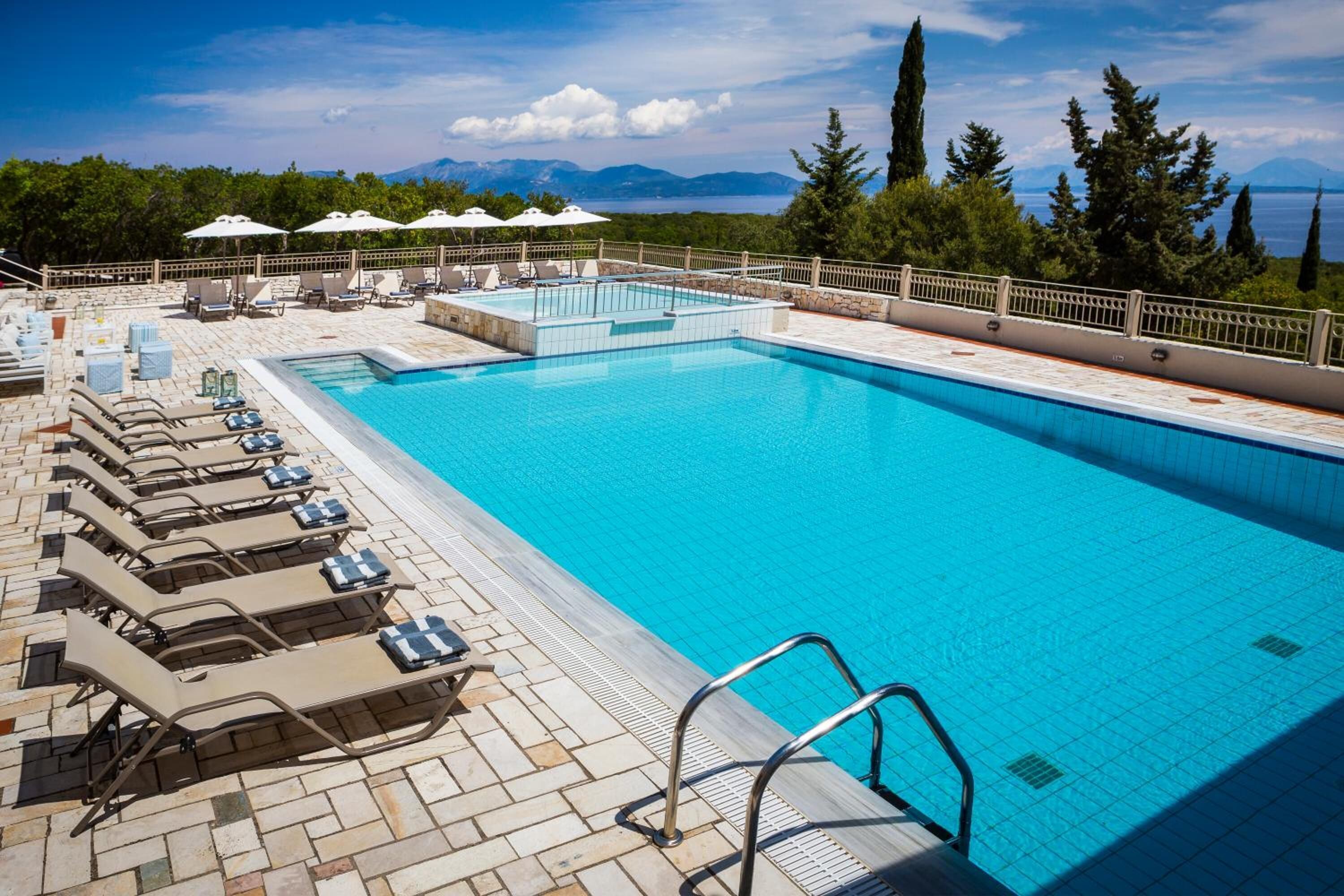 Uma piscina com espreguiçadeiras e guarda-sóis, cercada por árvores e montanhas ao fundo.