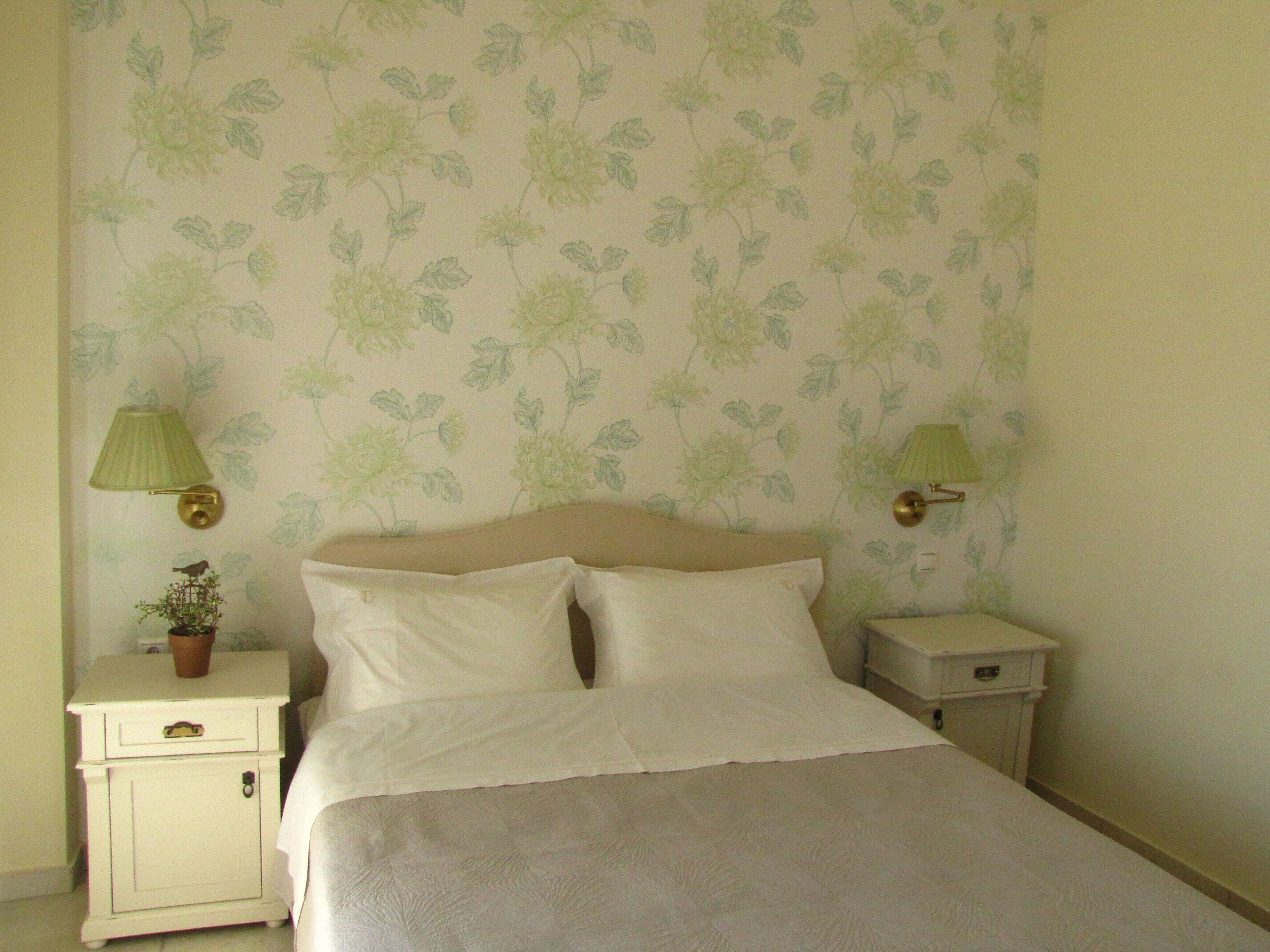 A bedroom with a bed, two nightstands, a lamp on each nightstand, and a wall with floral wallpaper.