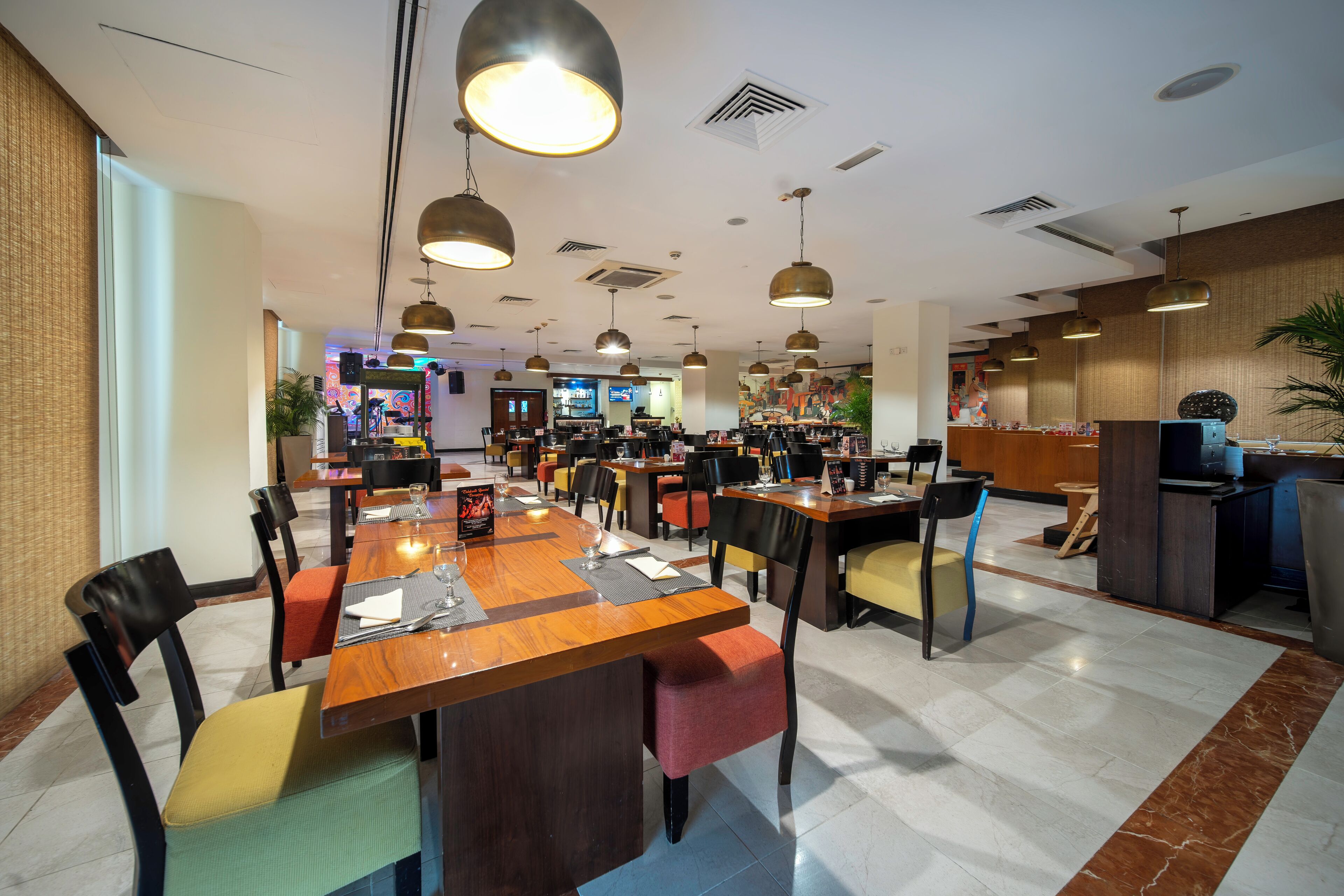 A modern restaurant with wooden tables and chairs, pendant lighting, and a central bar area.