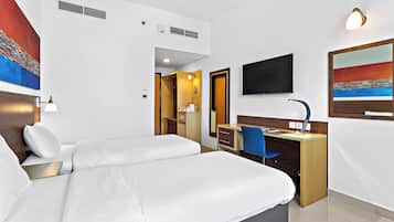 Ein Hotelzimmer mit Bett, Schreibtisch, Stuhl, Fernseher, Kunstwerken und einem durch eine geöffnete Tür einsehbarer Badezimmer.