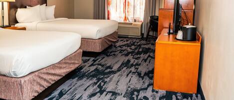 A hotel room with two beds, a desk, a chair, a lamp, and a television.