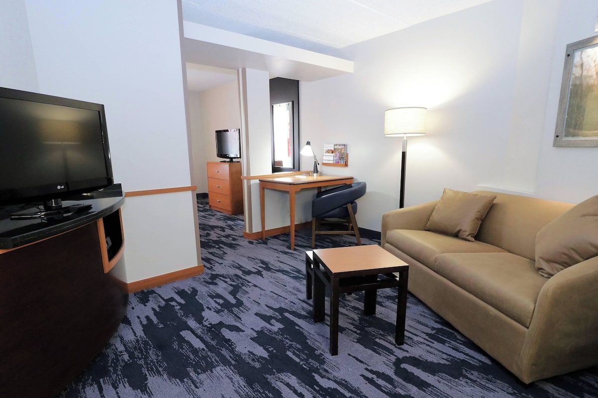 Ein Hotelzimmer mit Flachbildfernseher, Schreibtisch mit Stuhl, einer Couch und einer Lampe.