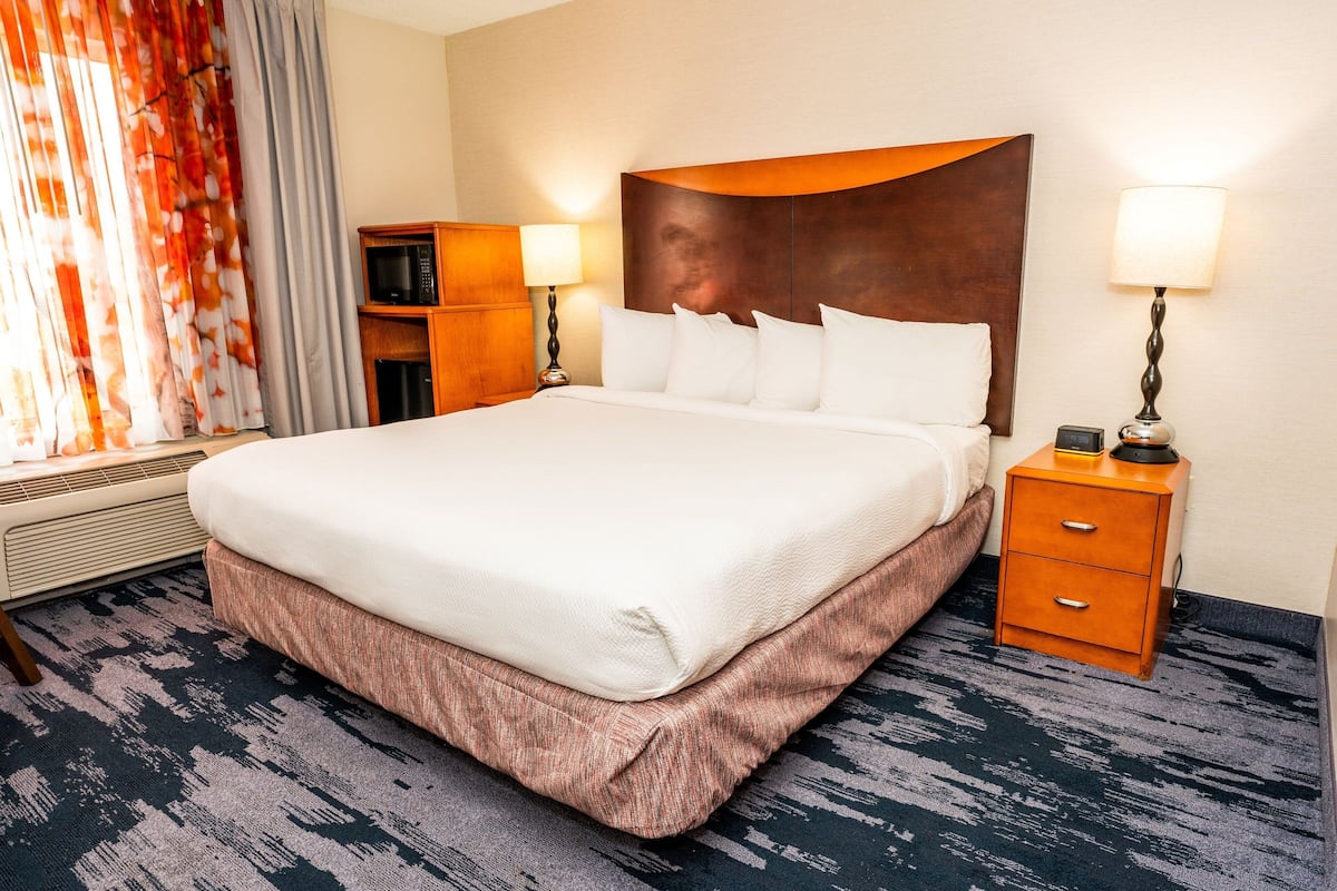 Ein Hotelzimmer mit einem großen Bett, einem Nachttisch mit Lampe, einer Mikrowelle und einem kleinen Schrank.