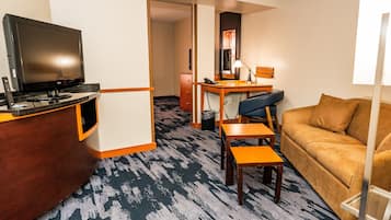 Una habitación de hotel con televisión, escritorio, silla, sofá y alfombra estampada.