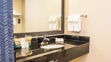 Un baño con lavamanos de superficie negra, un espejo y un perchero con toallas dobladas.