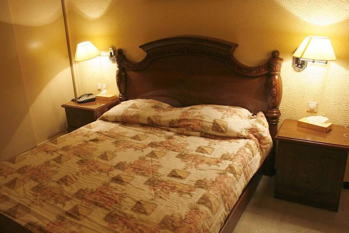 A neatly made bed with a floral-patterned bedspread, two bedside lamps, and a wooden headboard.
