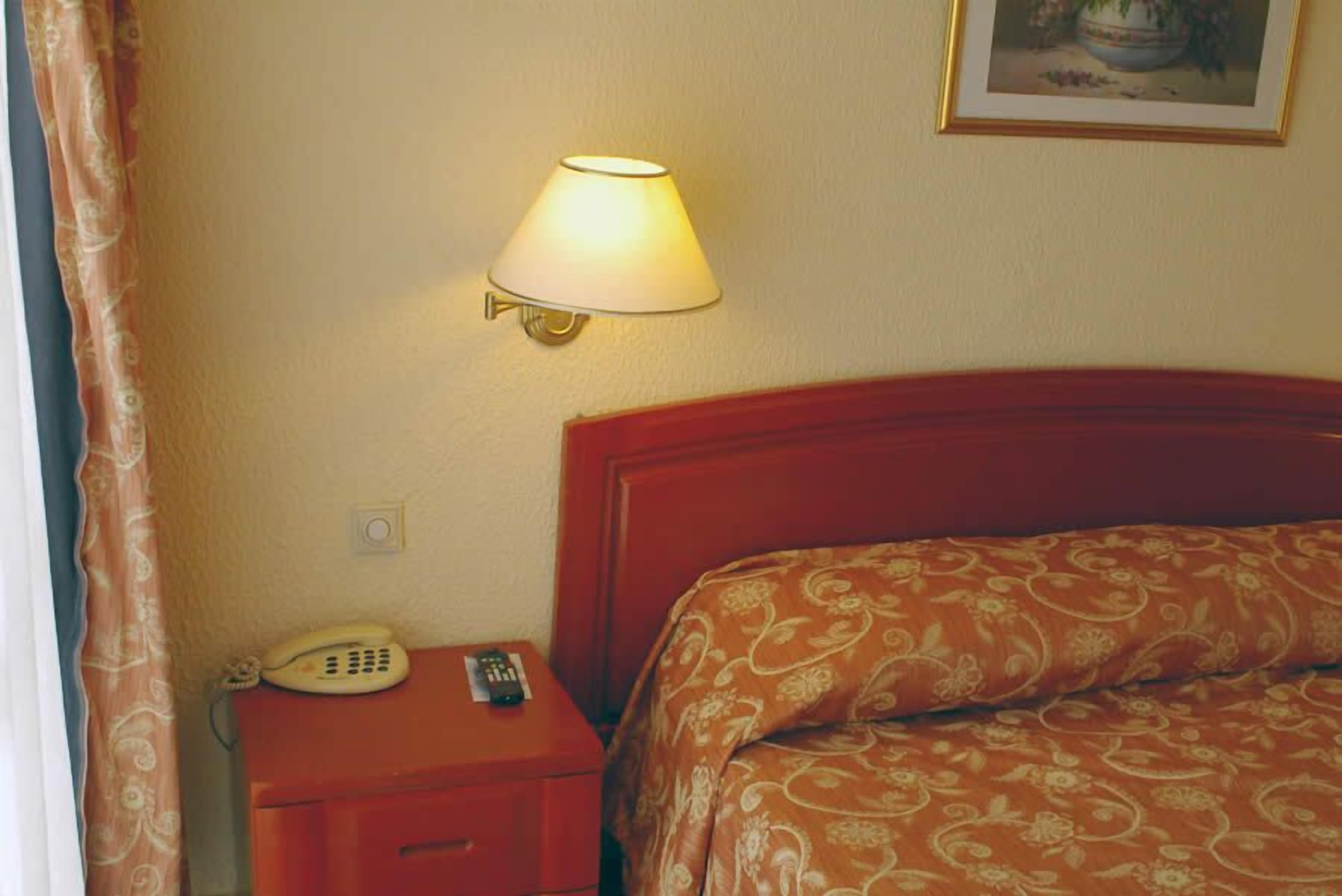 Ett hotellrum med en säng, ett nattduksbord med en lampa och en telefon.