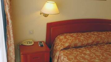 Ett hotellrum med en säng, ett nattduksbord med en lampa och en telefon.