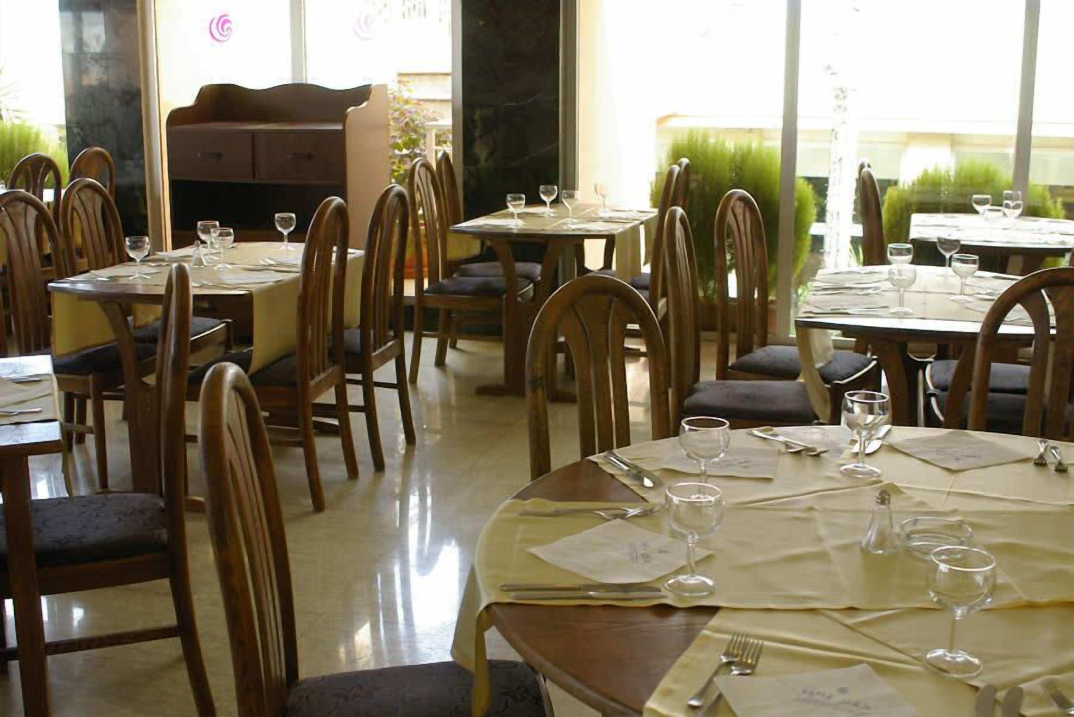 Un restaurante con mesas redondas y sillas de madera, cada conjunto con copas de vino, cubiertos y menús.