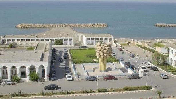 A coastal building with a parking lot and a large sculpture in front. - Safir Mazafran (Algiers)