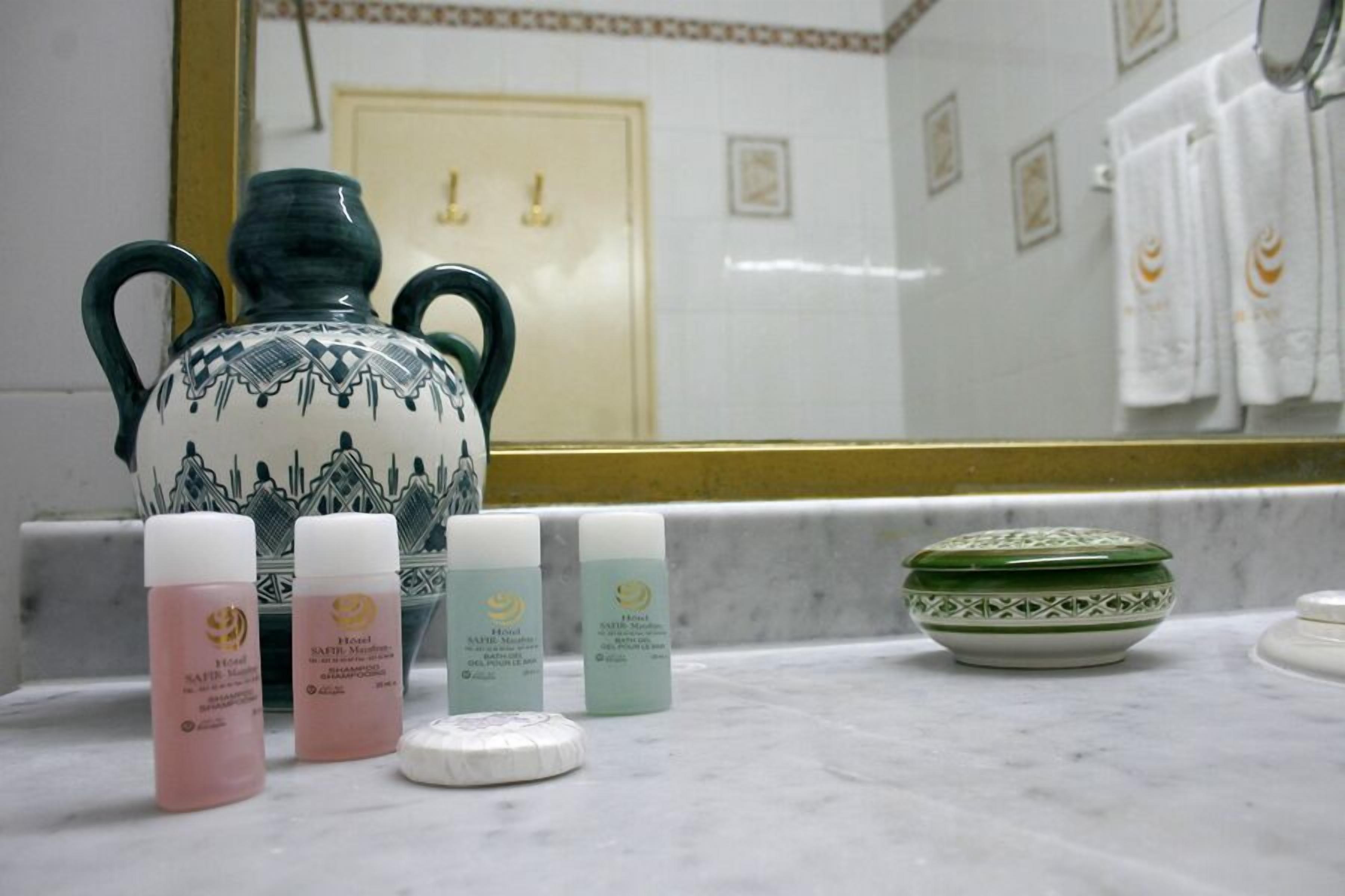 Een badkamer met een grote decoratieve vaas, verschillende shampoos en een groene kom op het aanrecht.
