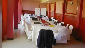Una sala de conferencias con una larga mesa, sillas blancas y una pizarra.