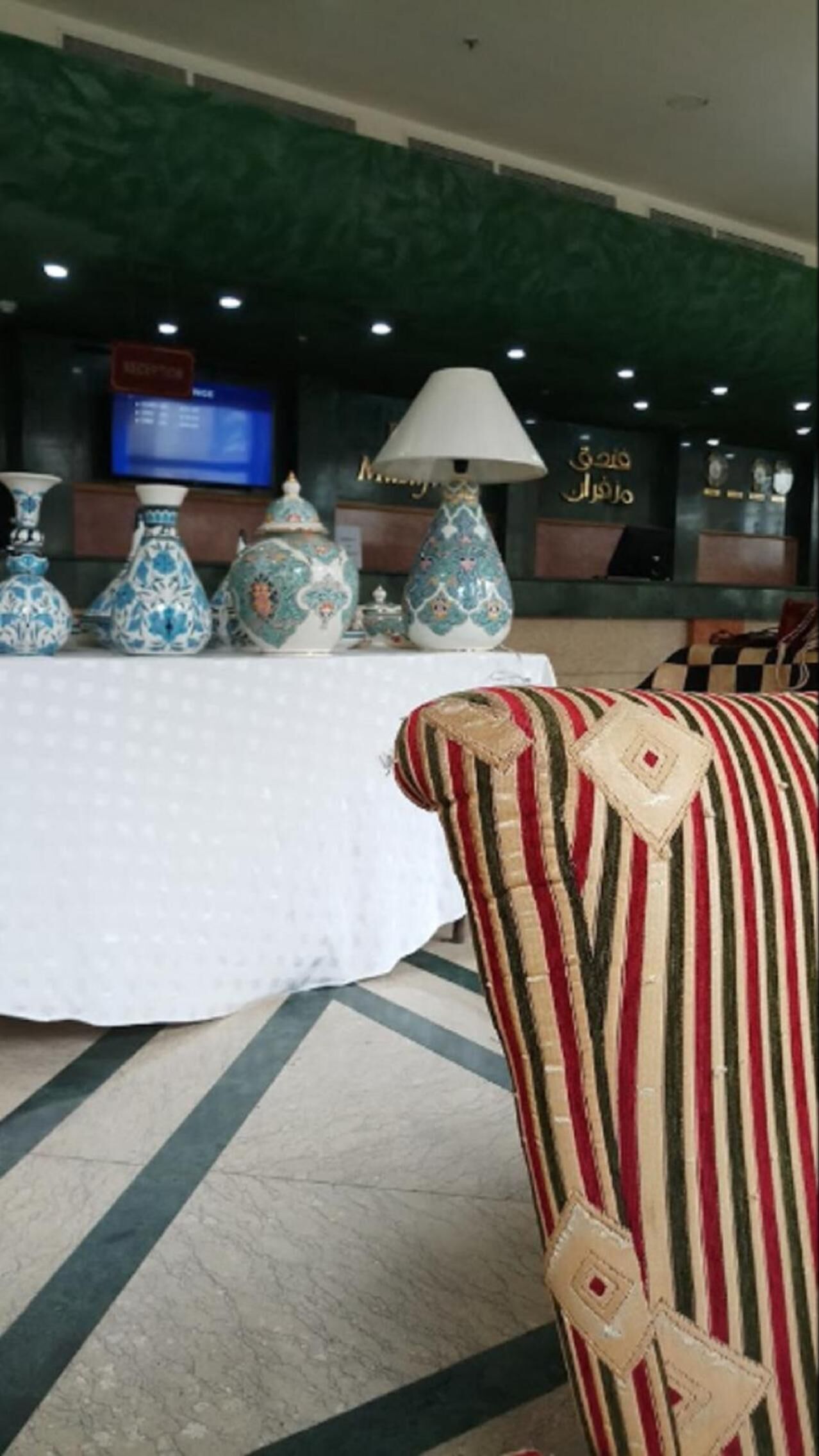 Een hal met een tafel waarop decoratieve vazen staan, een gestreept fauteuil en een televisiescherm op de achtergrond.