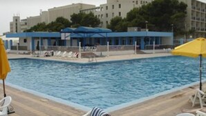 A swimming pool with lounge chairs and umbrellas, surrounded by buildings. - Safir Mazafran (Algiers)