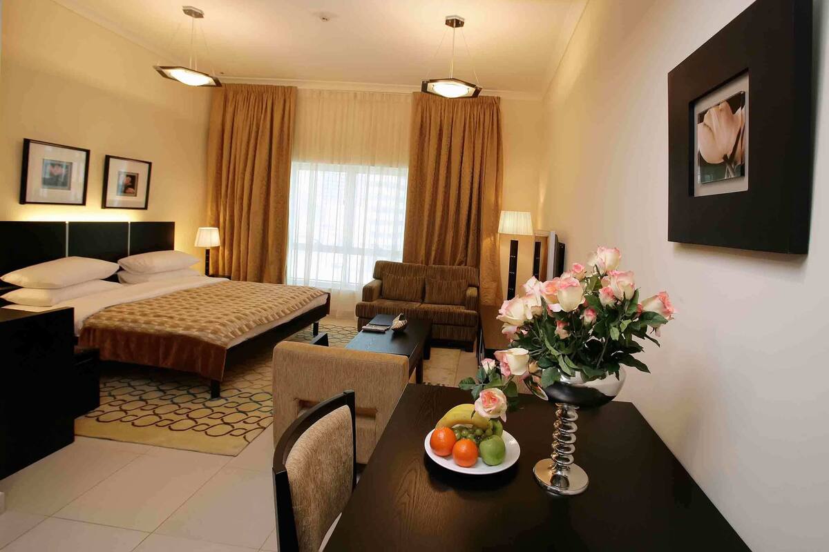 A hotel room with a bed, a sitting area with a chair and table, a desk, and a window with curtains.