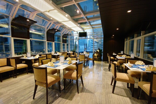 Un restaurant moderne doté d’un plafond haut et de grandes fenêtres, offrant une vue sur le paysage urbain.