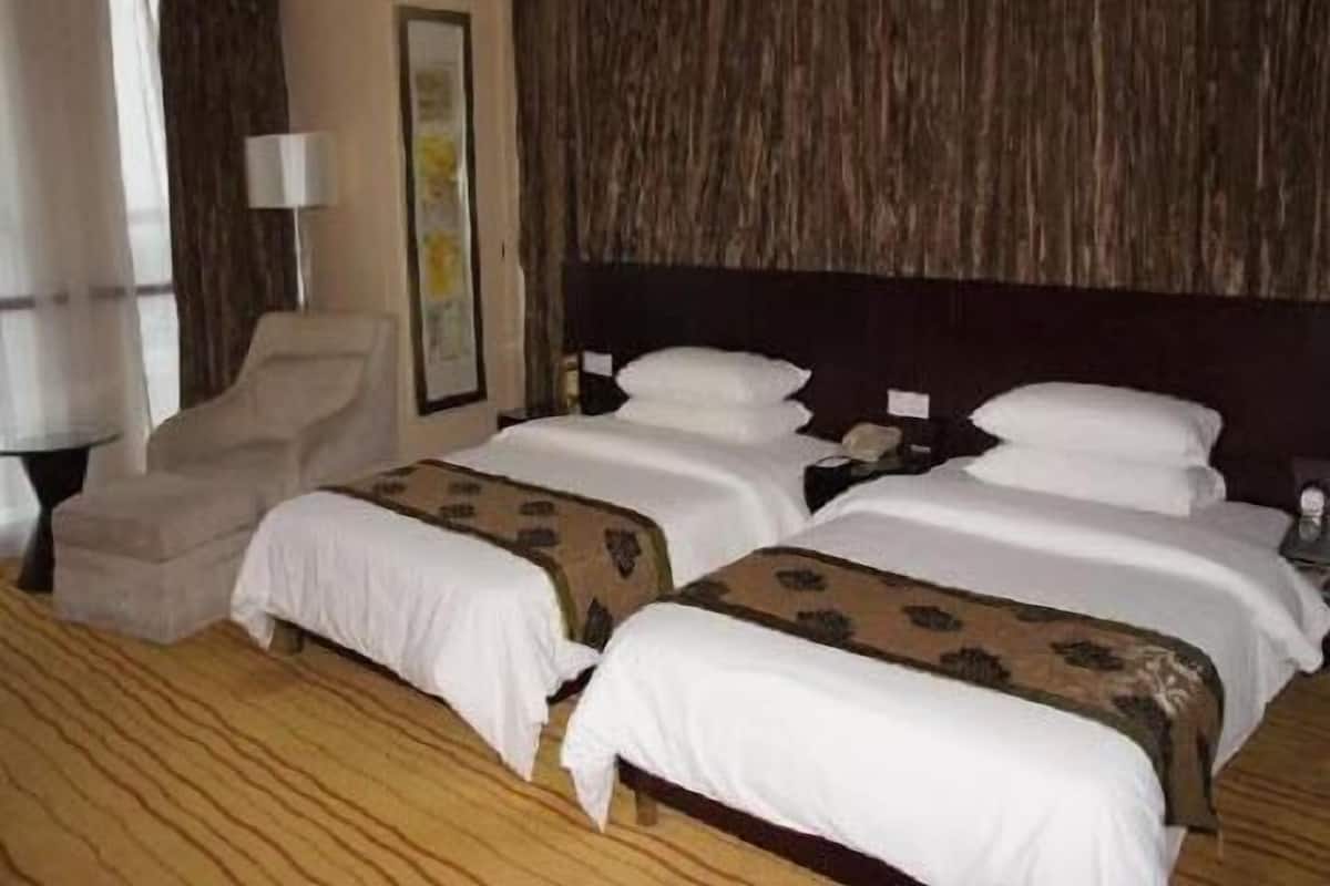 Quarto de hotel com duas camas, uma cadeira, uma mesa de cabeceira e uma luminária.