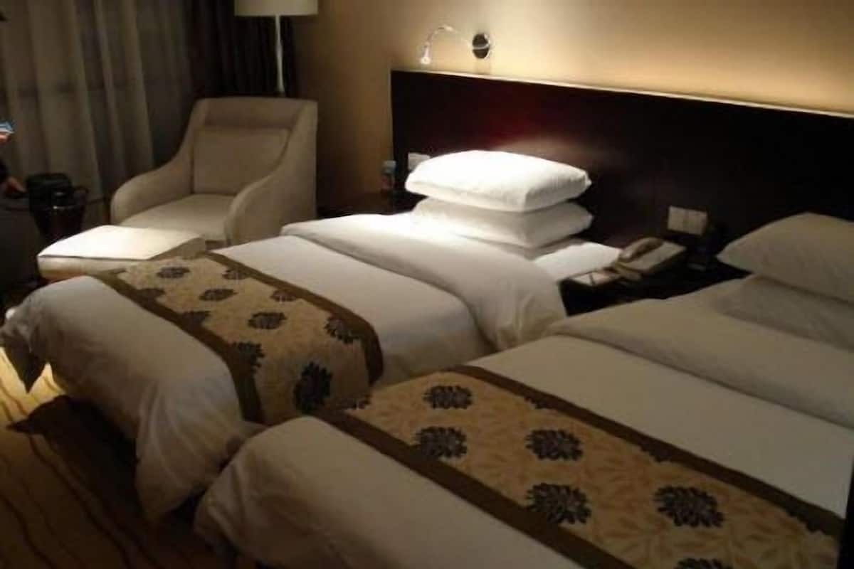 Quarto de hotel com duas camas, uma cadeira, uma mesinha de cabeceira e um abajur.