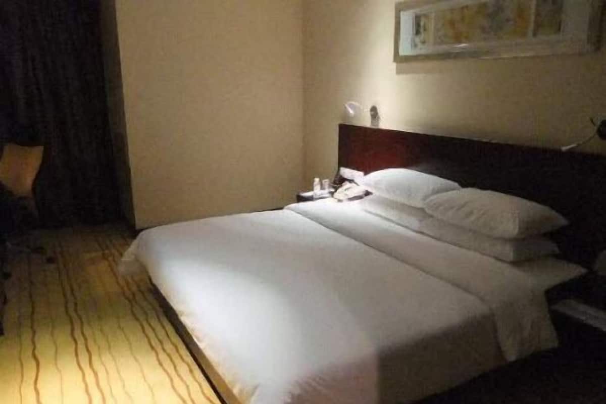 Quarto de hotel com uma cama grande, uma mesa de cabeceira e uma luminária fixada na parede.