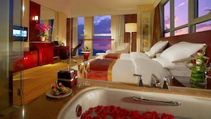 A hotel room with a large bed, a sitting area with a red sofa, a desk with a computer, a large window with a view of the sky, and a bathroom with a bathtub. - Nanjing New Century Hotel (Nanjing)