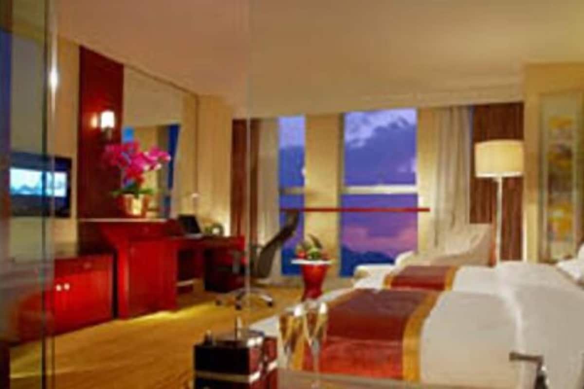 Quarto de hotel com uma cama grande, uma escrivaninha, uma cadeira e vista para o céu pela janela.