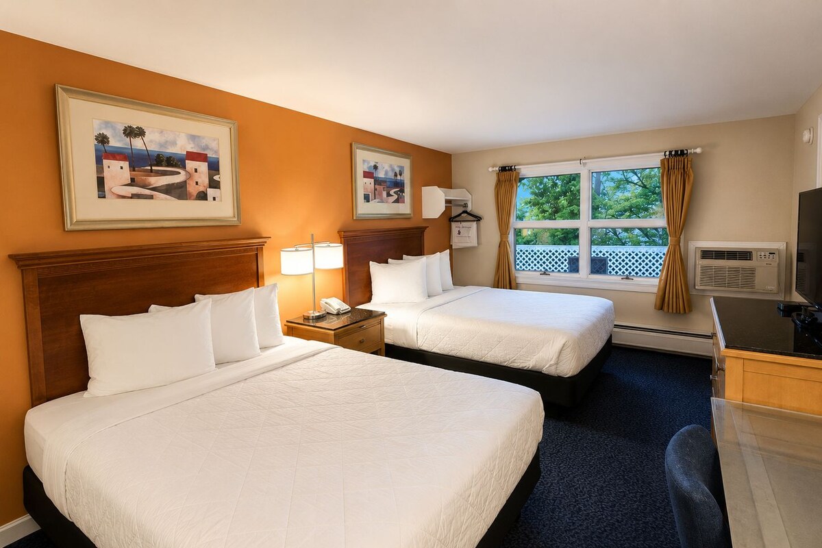 Habitación de hotel con dos camas, un escritorio, un televisor y una ventana con cortinas.