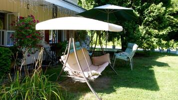 Une terrasse avec une chaise suspendue, une table et un parasol.