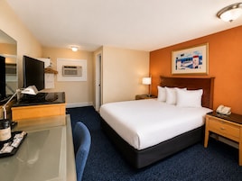 Habitación de hotel con cama, mesitas de noche, escritorio con lámpara, televisor y un cuadro en la pared.