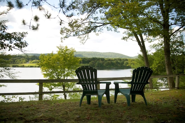Two Adirondack chairs facing a lake with a wooden deck and a view of a hilly landscape. - Sunset Motor Inn (West Lebanon)