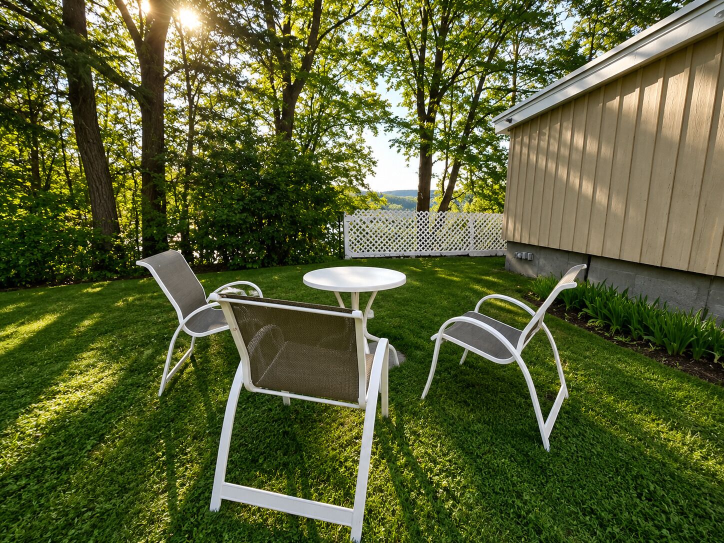 Un espacio al aire libre con una mesa y dos sillas, rodeado de césped cuidado y árboles.