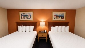 A hotel room with two beds, a nightstand with a lamp, and two framed pictures on the wall.