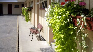 A row of hotel rooms with a covered outdoor area, a bench, and potted plants along the wall.