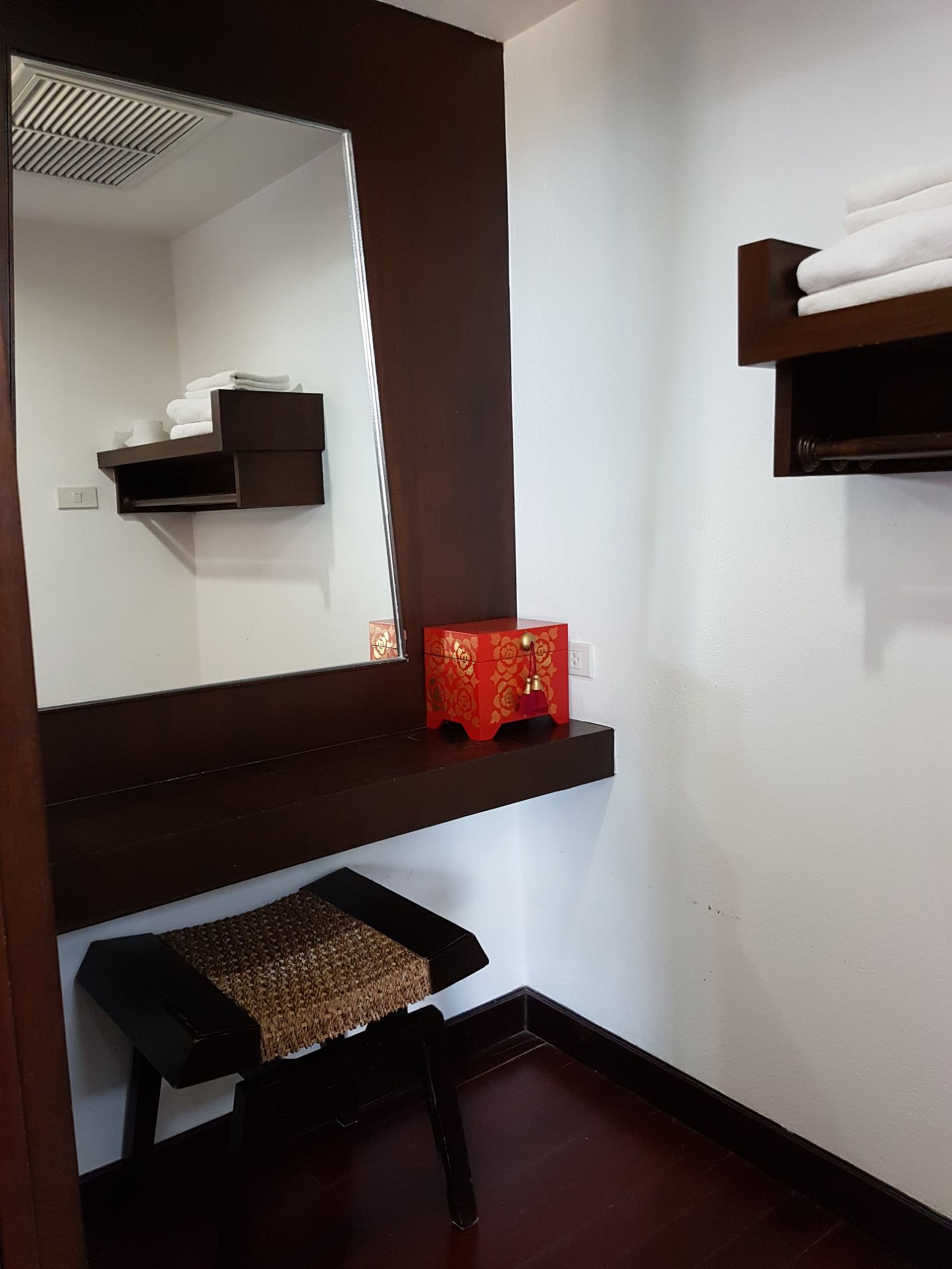 A bathroom with a dark wooden vanity, a mirror, a towel rack, and a red decorative box.