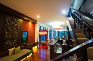 A modern hotel lobby with a wooden bench, a red and white partition, and a staircase. - Nicha Hua Hin Hotel (Hua Hin)