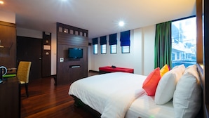 Una habitación de hotel con una cama grande, televisión, escritorio y ventana con cortinas.