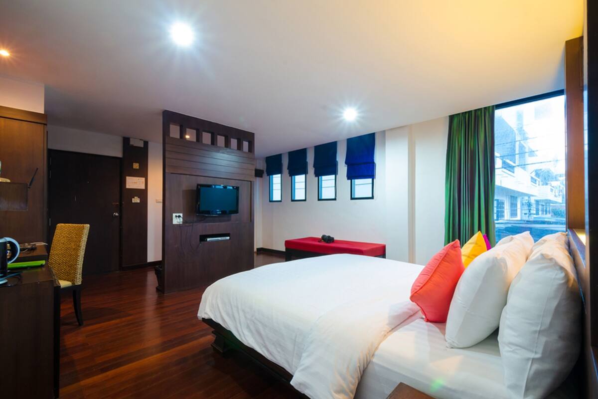 Une chambre d’hôtel avec un grand lit, une télévision, un bureau et une fenêtre avec des rideaux.