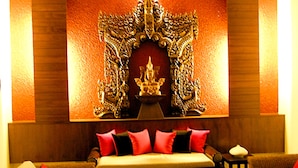 Una habitación con cabecera de madera, pared con estampado rojo y negro, y una estatua dorada decorativa.