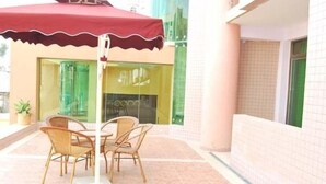 Een terras met rieten stoelen en een rode parasol.