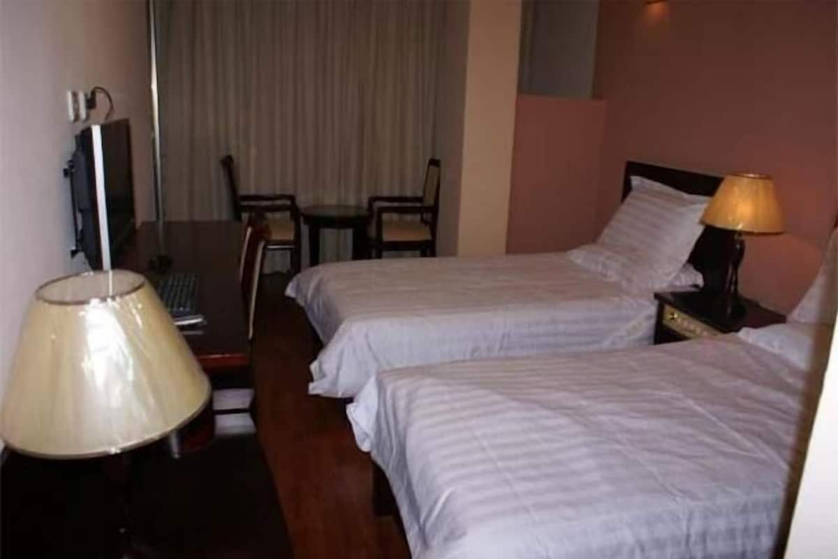 Habitación de hotel con dos camas individuales, un escritorio con silla, televisión y lámpara.