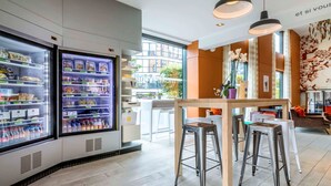 Un hall d’hôtel moderne doté d’une vitrine réfrigérée, de tabourets de bar et d’un espace salon offrant une vue sur la ville.