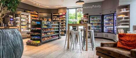 Un espace de vente moderne comprenant un rayon boulangerie, un coin salon avec un canapé et des fauteuils, et une variété de produits exposés sur des étagères.