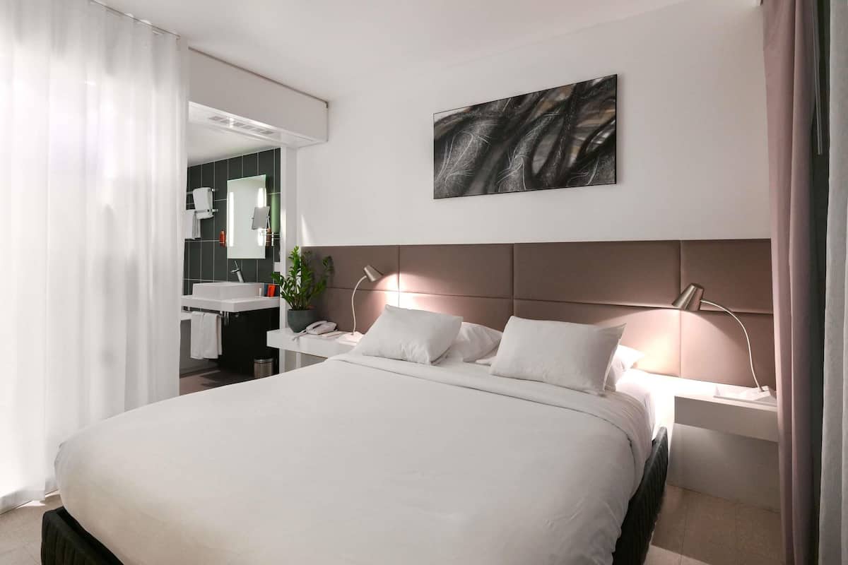 Une chambre d’hôtel moderne avec un grand lit, des tables de chevet, un miroir et une œuvre d’art accrochée au mur.