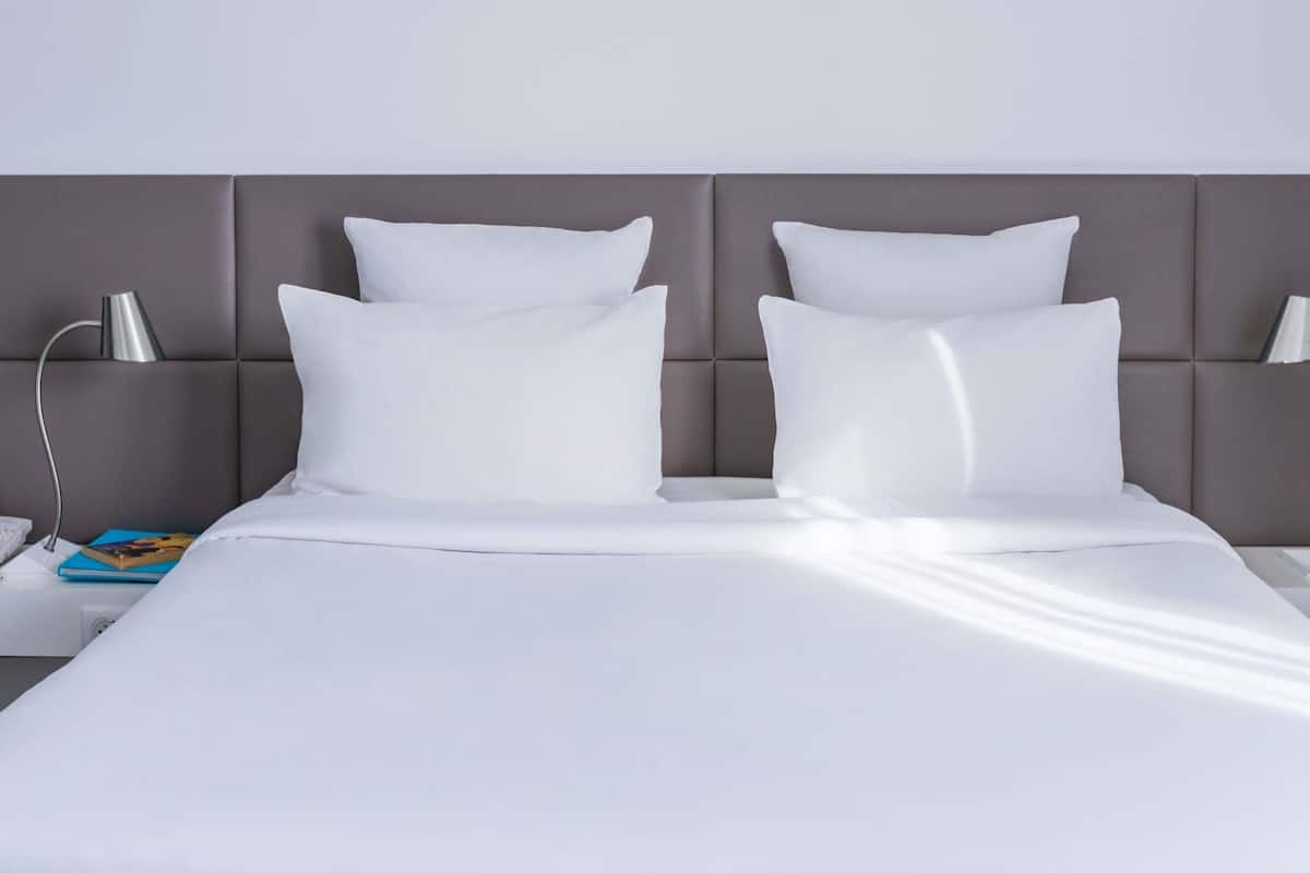 A neatly made bed with white linens and pillows, a bedside lamp, and a book on the nightstand.