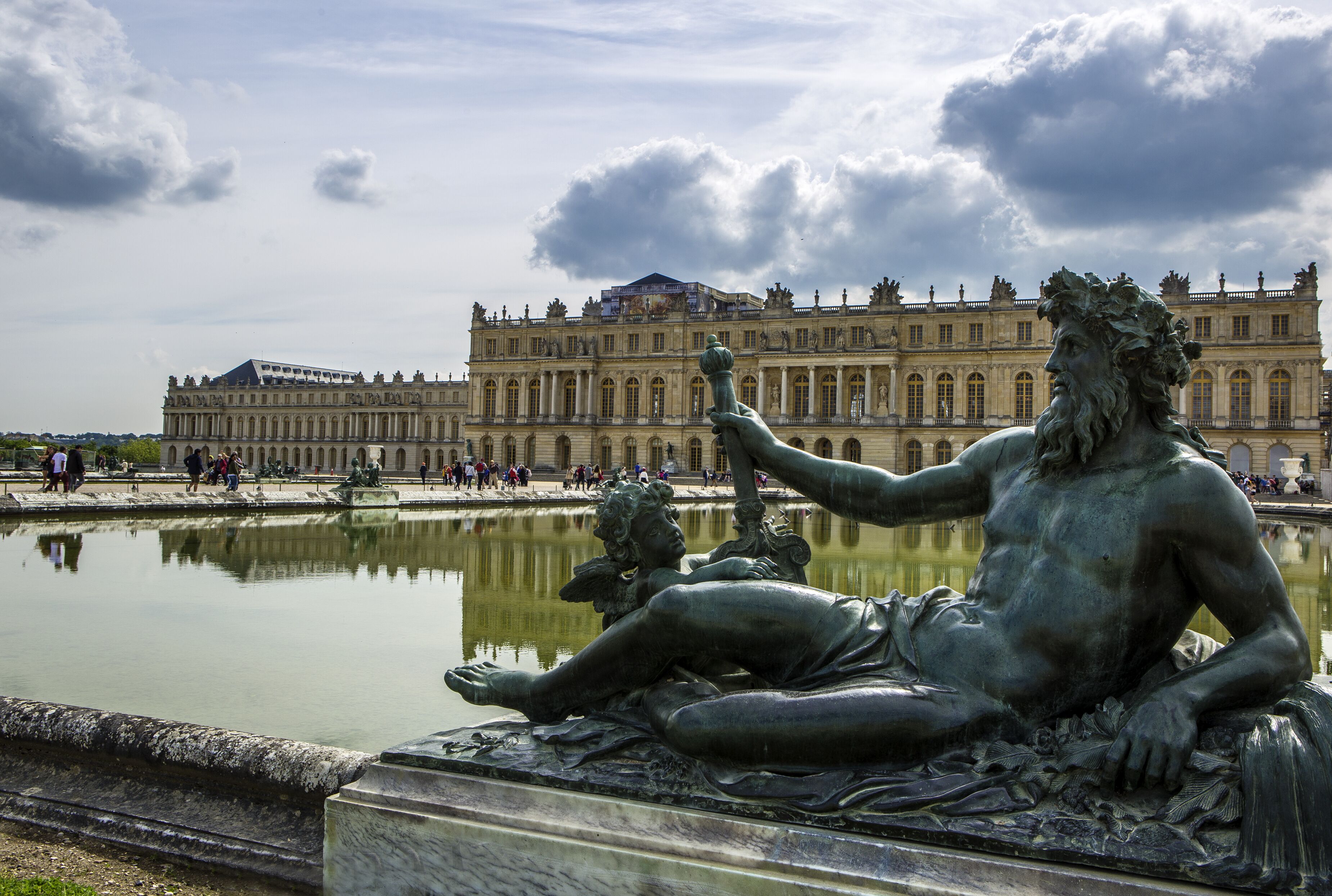 A statue of a reclining figure by a reflective water body with a grand building in the background.