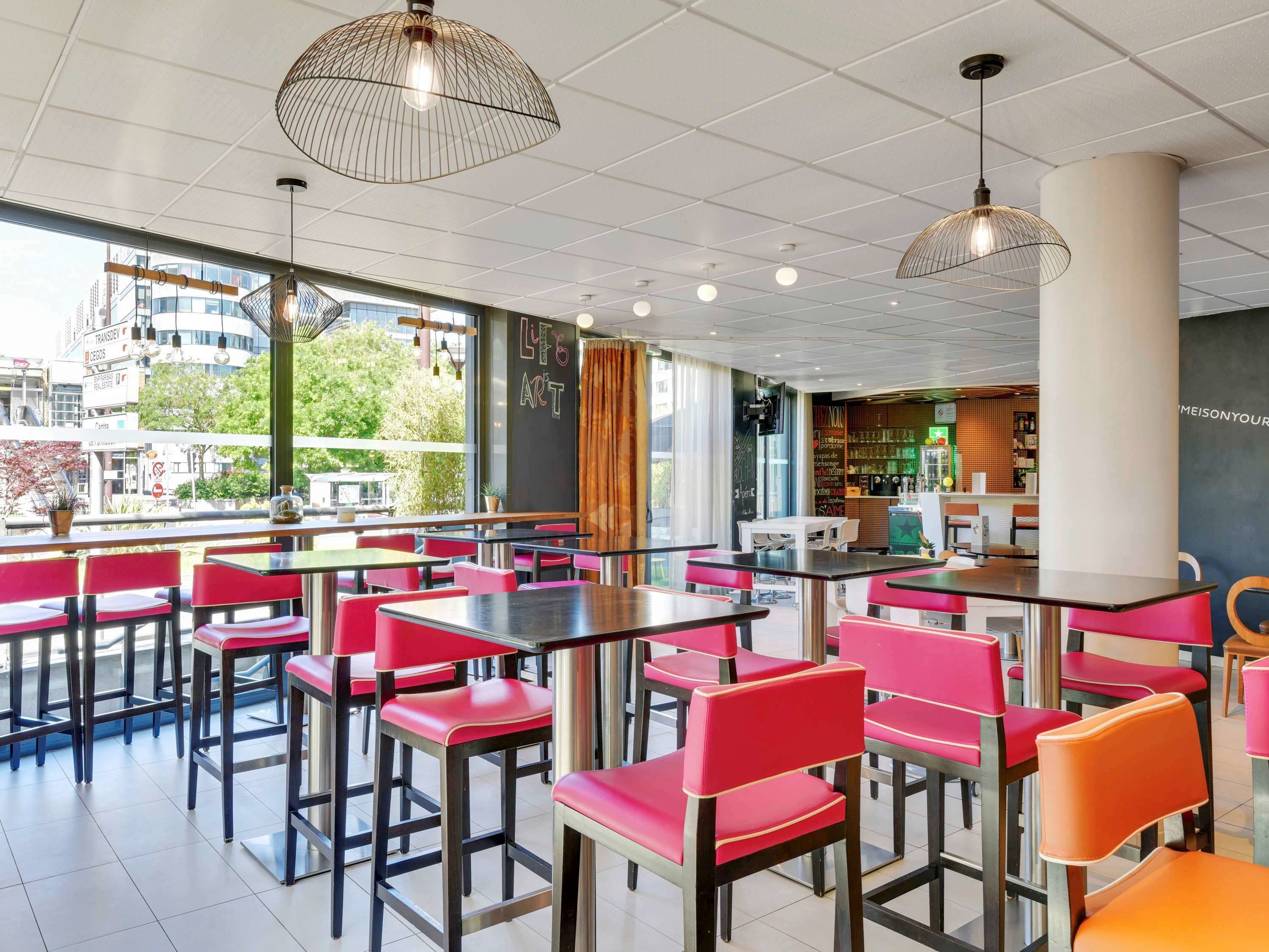 Un café moderne avec des chaises rouges et orange, des tables noires et des lampes suspendues.