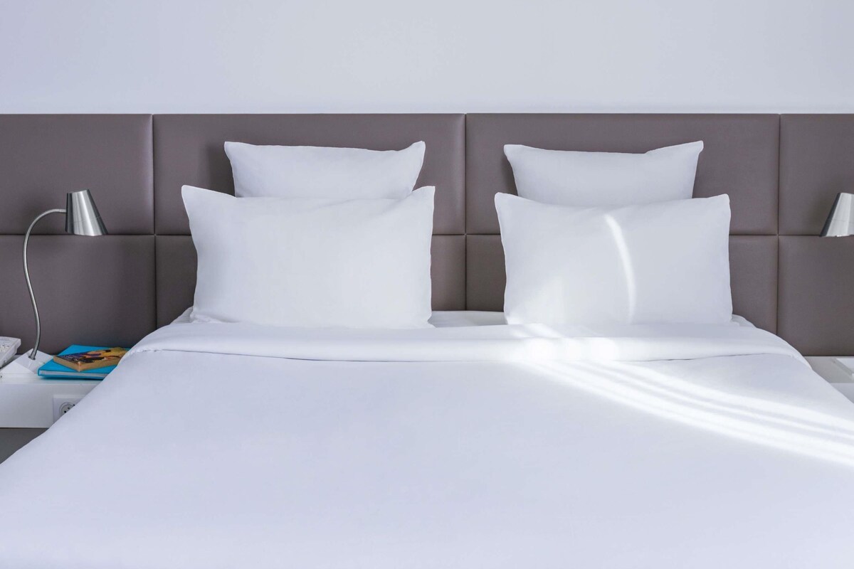 A neatly made bed with white linens and pillows, a bedside lamp, and a book on the nightstand.