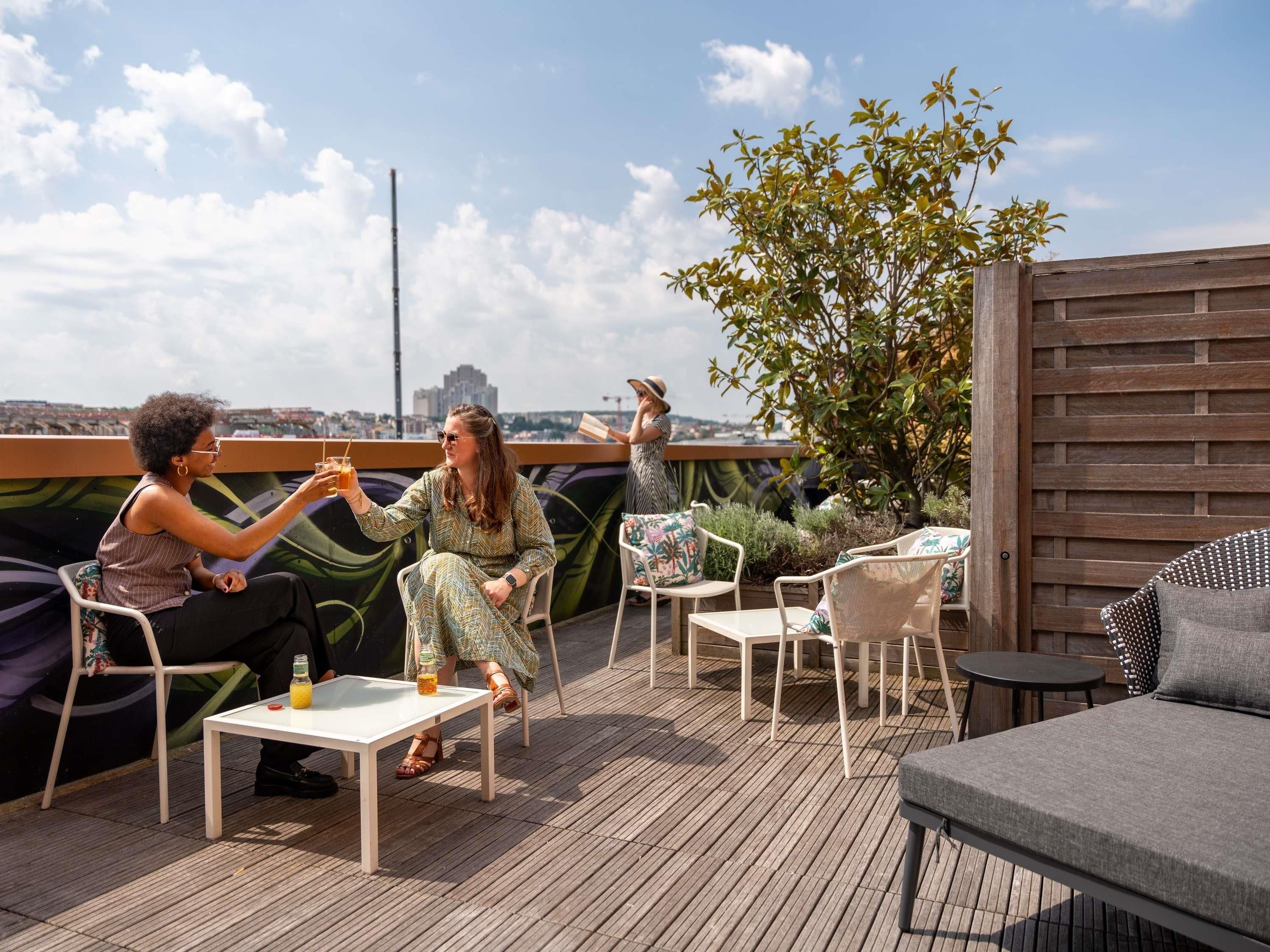 A rooftop terrace with outdoor seating, a city view, and a wooden fence.