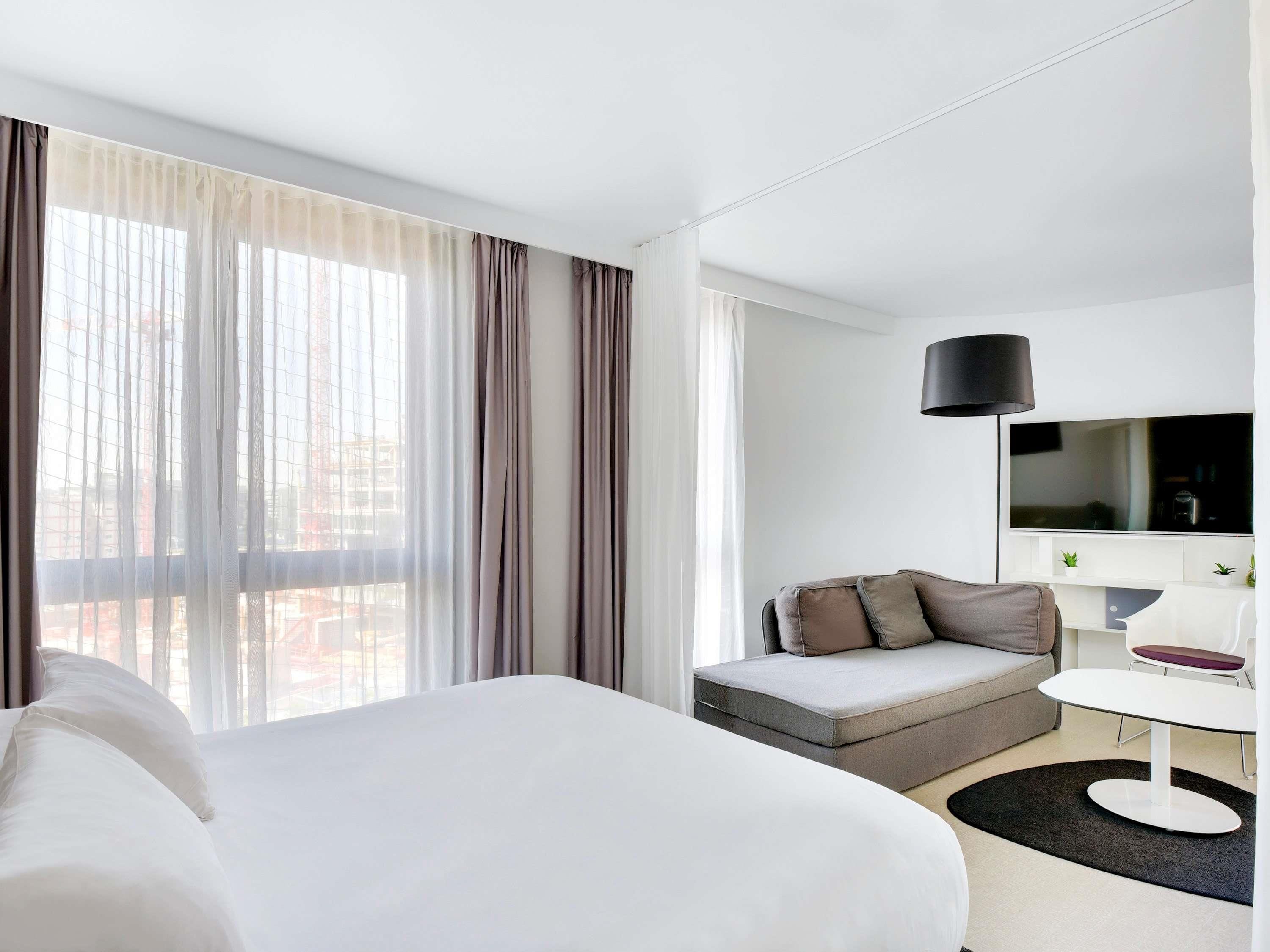 A modern hotel room with a large bed, a sofa, a small table, and a TV.